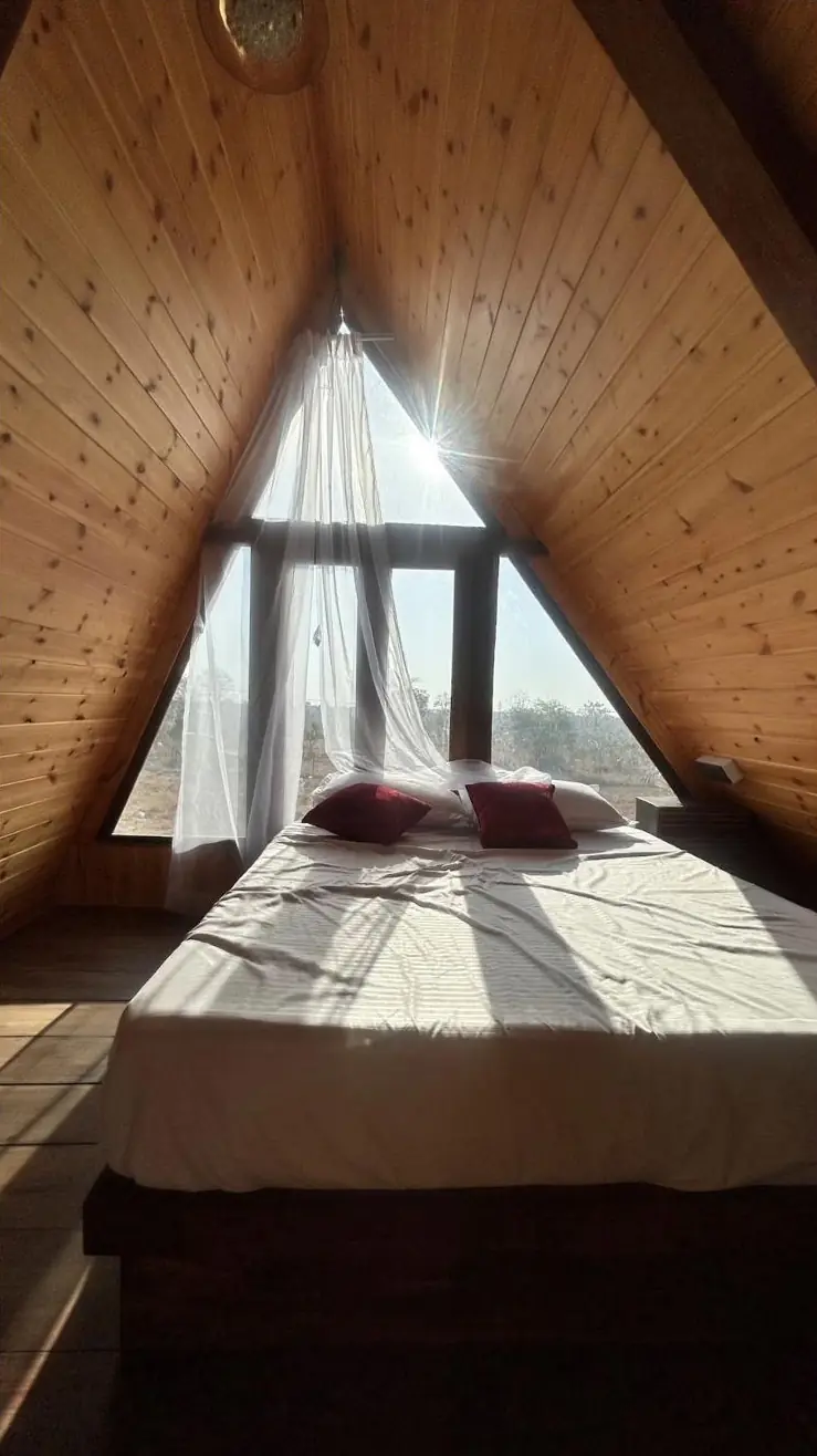 King bed in the loft of an A-frame cottage, sunlight through the triangle window